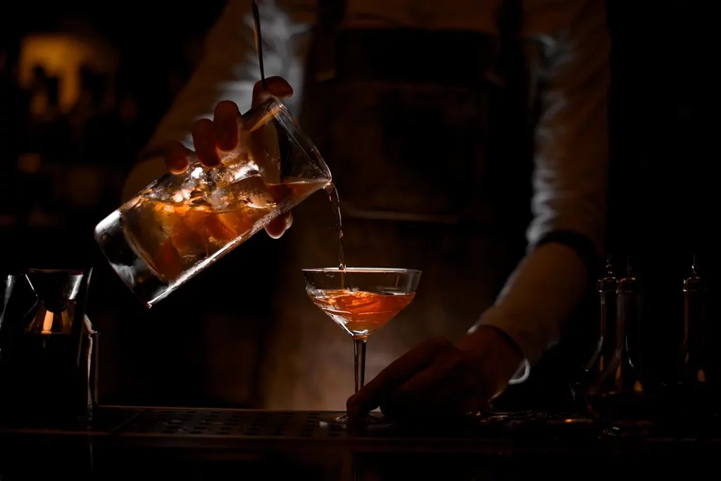 A bartender pouring a drink in a shadowy bar.