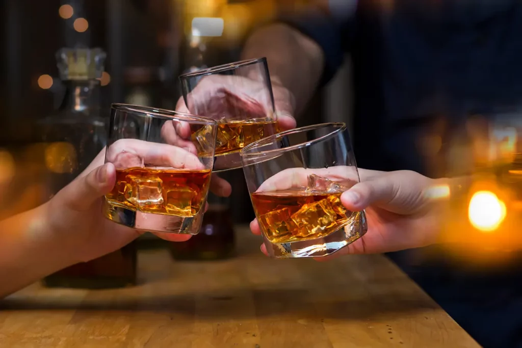 Three people holding short glasses of liquor.