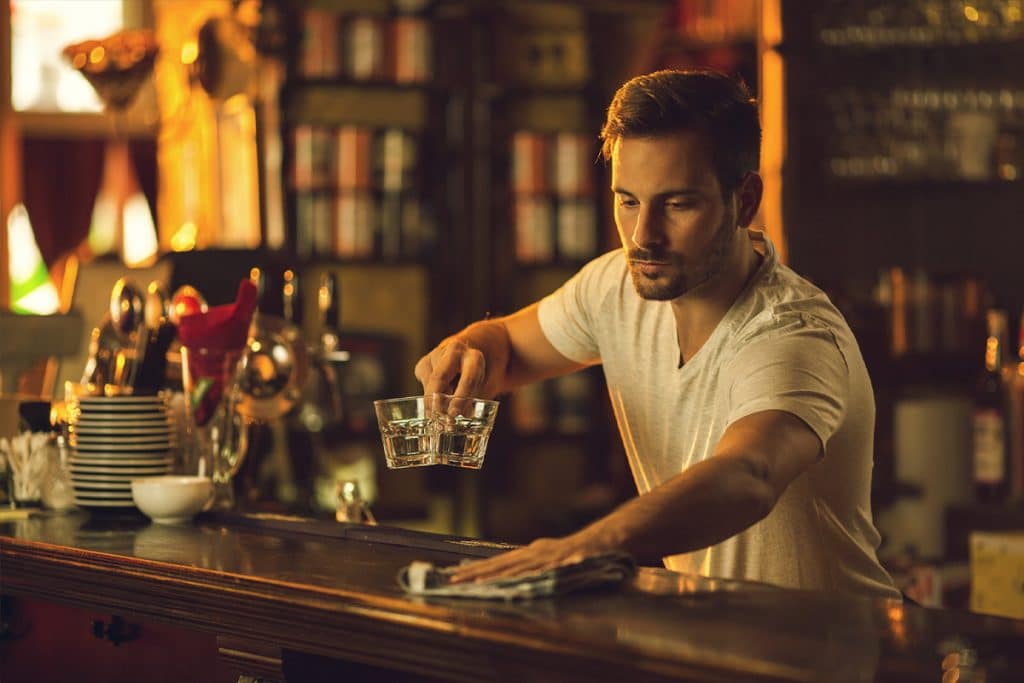 A bartender clears and wipes down a bar.