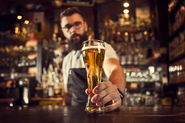 A bartender serves a freshly poured beer across the bar.