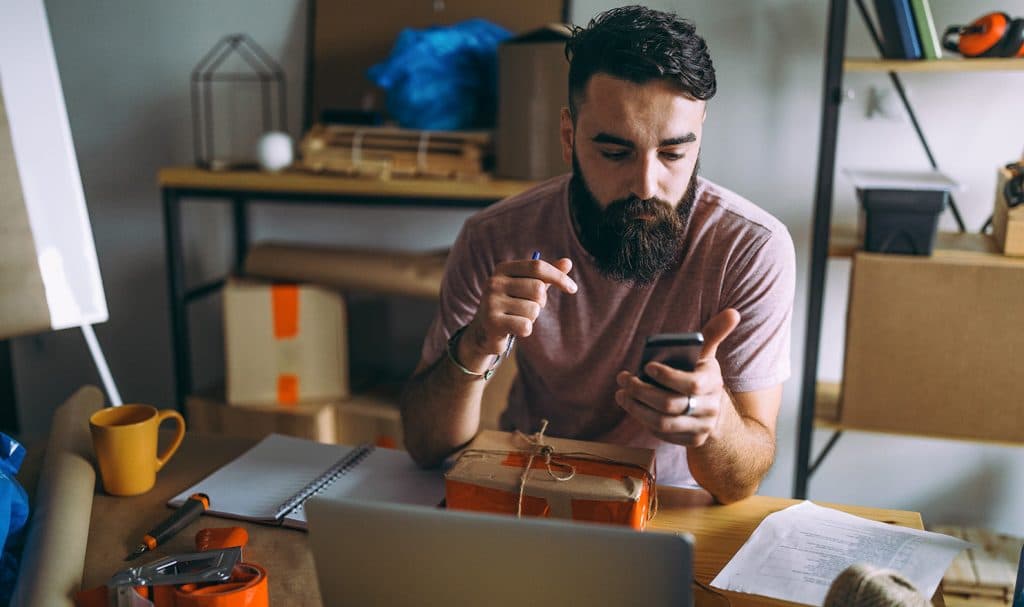 An eBay seller looks at his phone to let his buyer know he is about to ship their package.