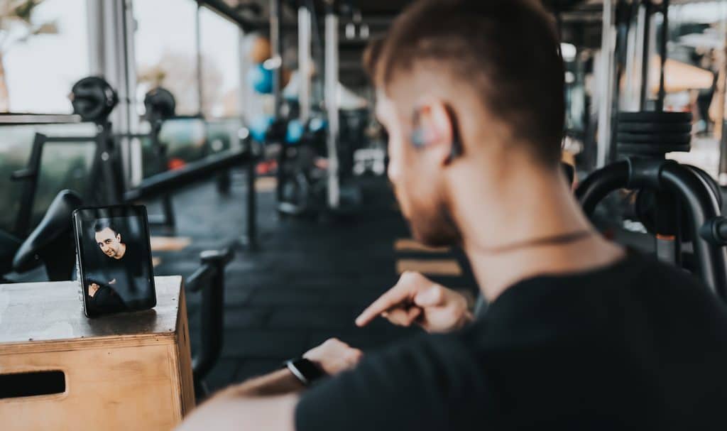 A trainer is on a virtual call with a client while he trains in the gym.