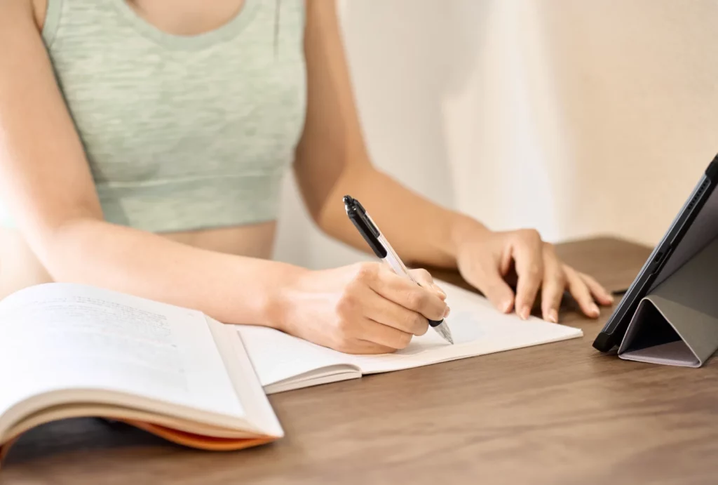 Woman in light green sports bra studying a textbook and taking notes.