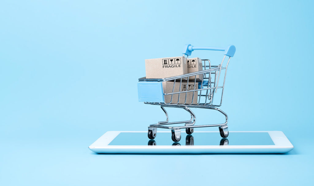 A mini shopping cart with two cardboard boxes inside is sitting on top of a tablet on a blue background showing product liability for sellers.