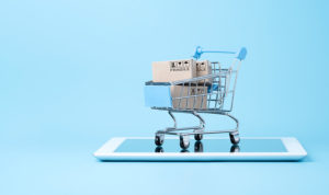 A mini shopping cart with two cardboard boxes inside is sitting on top of a tablet on a blue background showing product liability for sellers.
