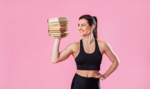 A personal trainer holding a stack of books against a pink background.