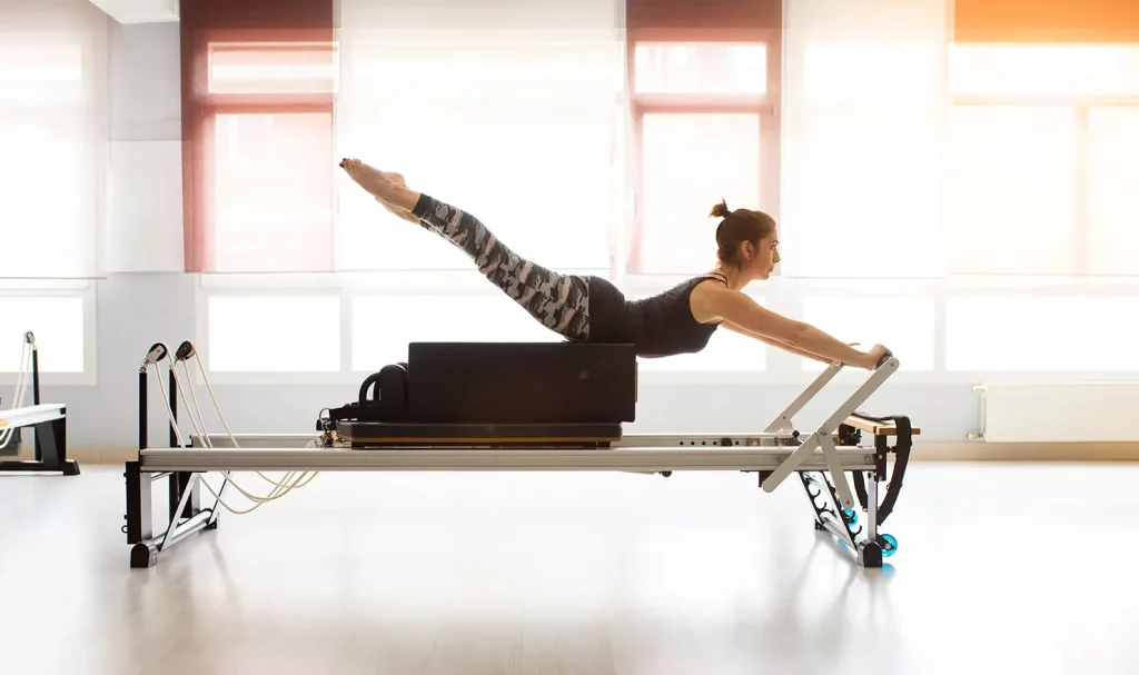 Pilates teacher using a reformer in a studio with natural lighting.