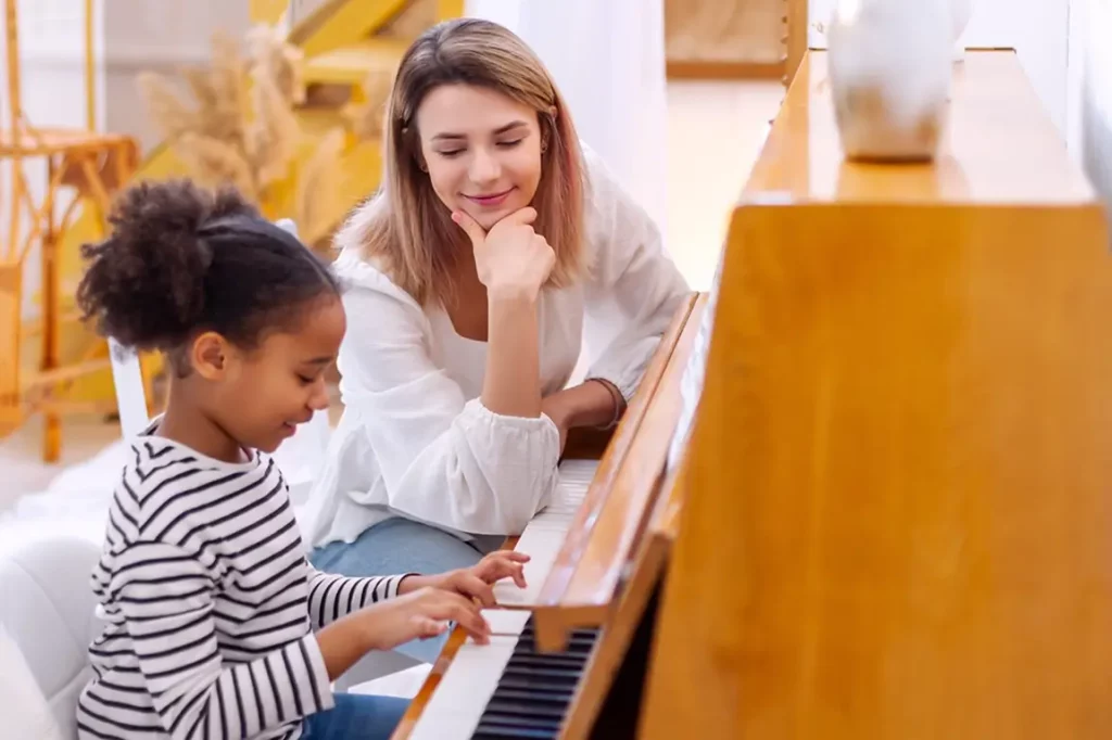 Music teacher sitting at the piano with her student who is practicing playing notes.