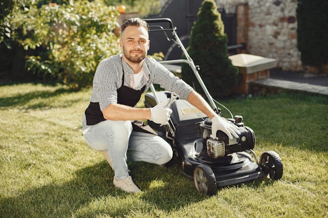 a lawn care employee holds a thumbs up sign next a lawn mower