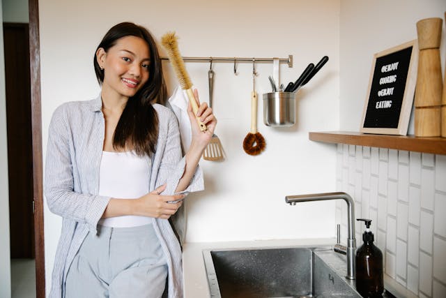 a smiling woman stands in a kitchen holding up a cleaning tool