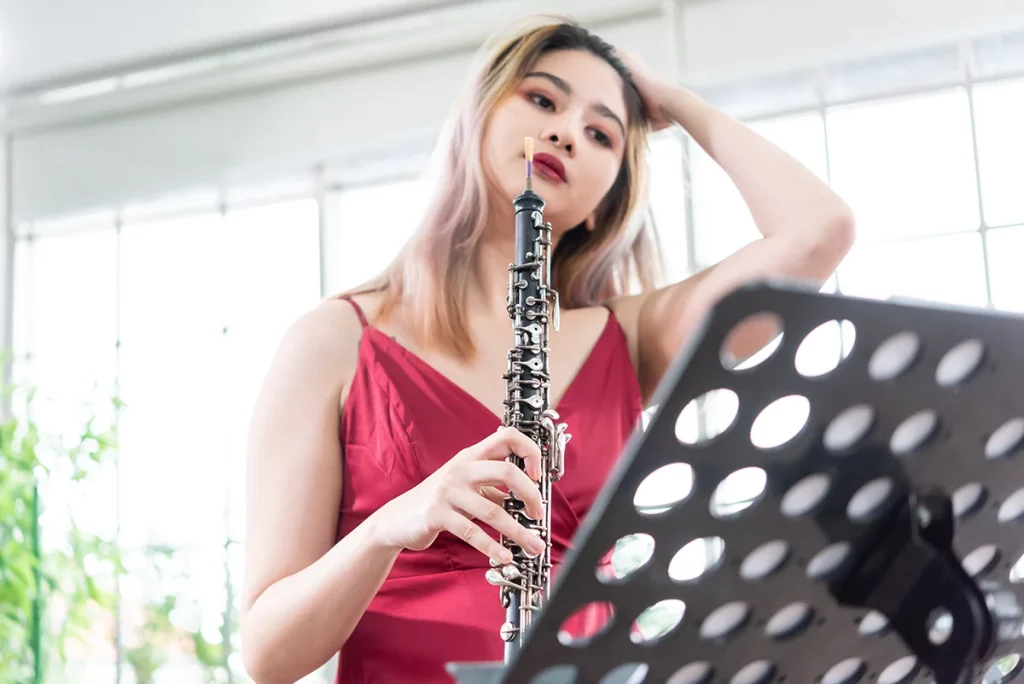 A woman in a burgundy dress playing the oboe.