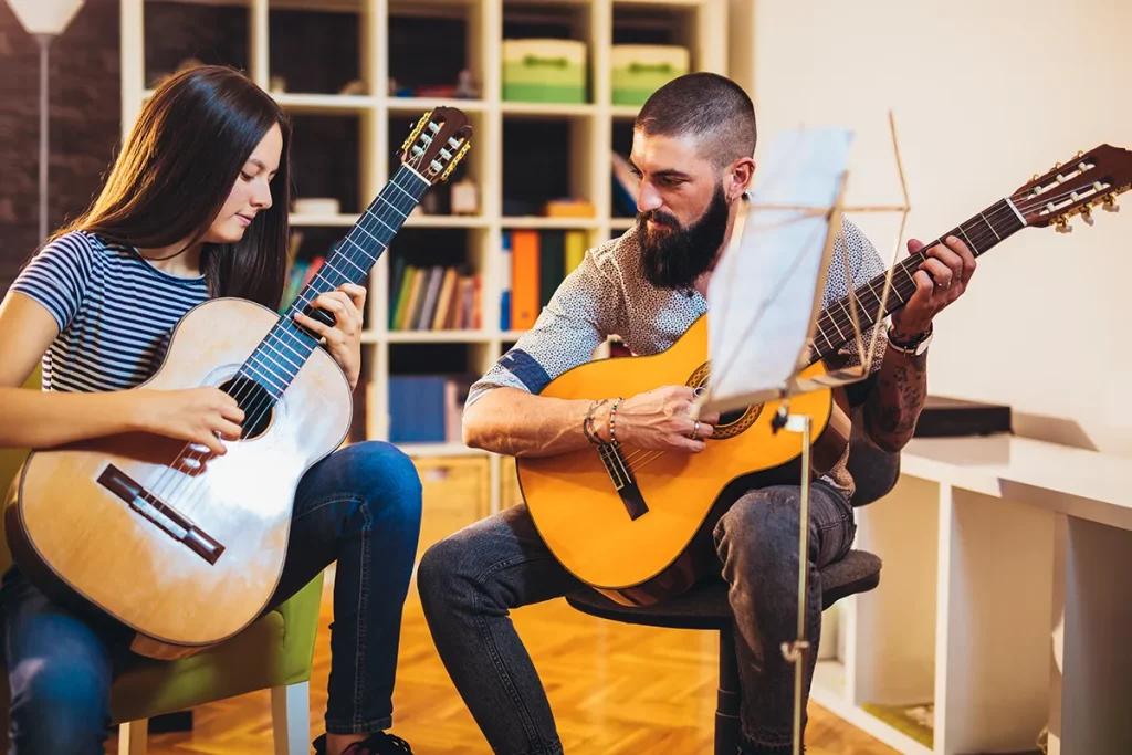 A man teaching a young girl how to play chords on a guitar during a music lesson.