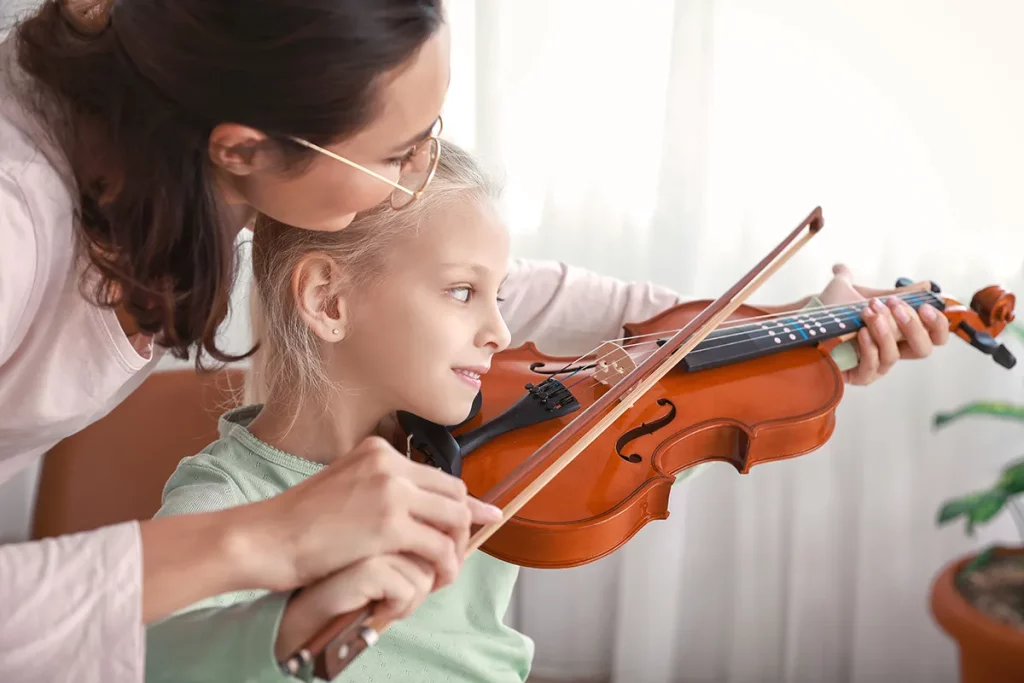 A private music teacher giving violin lessons to a young girl inside her home.