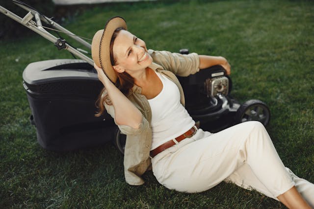 a woman sits smiling next to a lawn mower