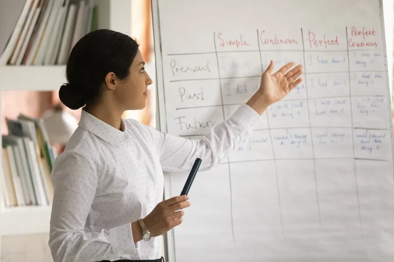 A tutor pointing to a whiteboard while holding a black marker.