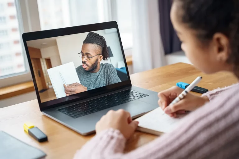 A young girl sitting at a desk in front of her laptop working with a virtual tutor.