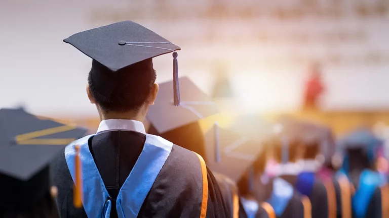 A shot of a college graduate from behind wearing a cap and gown at a graduation ceremony.