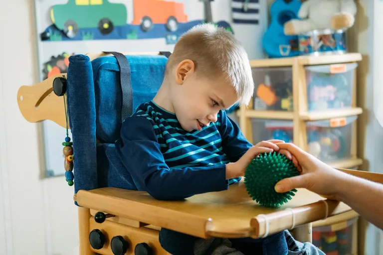 A young boy with cerebral palsy plays with a sensory toy in a classroom.