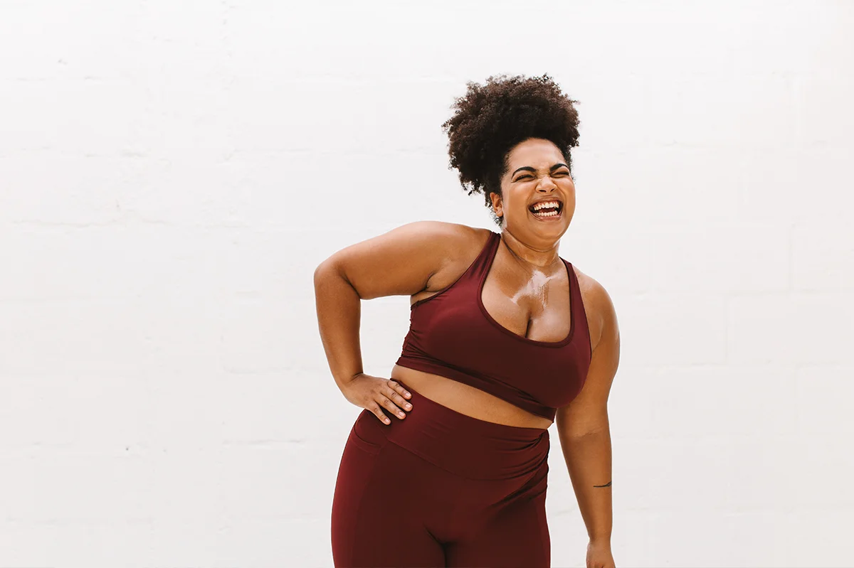 Woman in burgundy athletic leggings and sports bra laughing after working out.