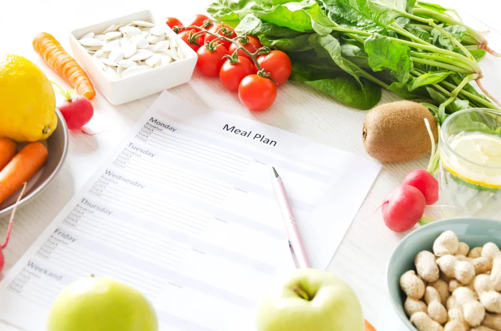 A white sheet of paper with black lettering, displaying a weekly meal plan template, sitting on a white counter surrounded by various vegetables and nuts.