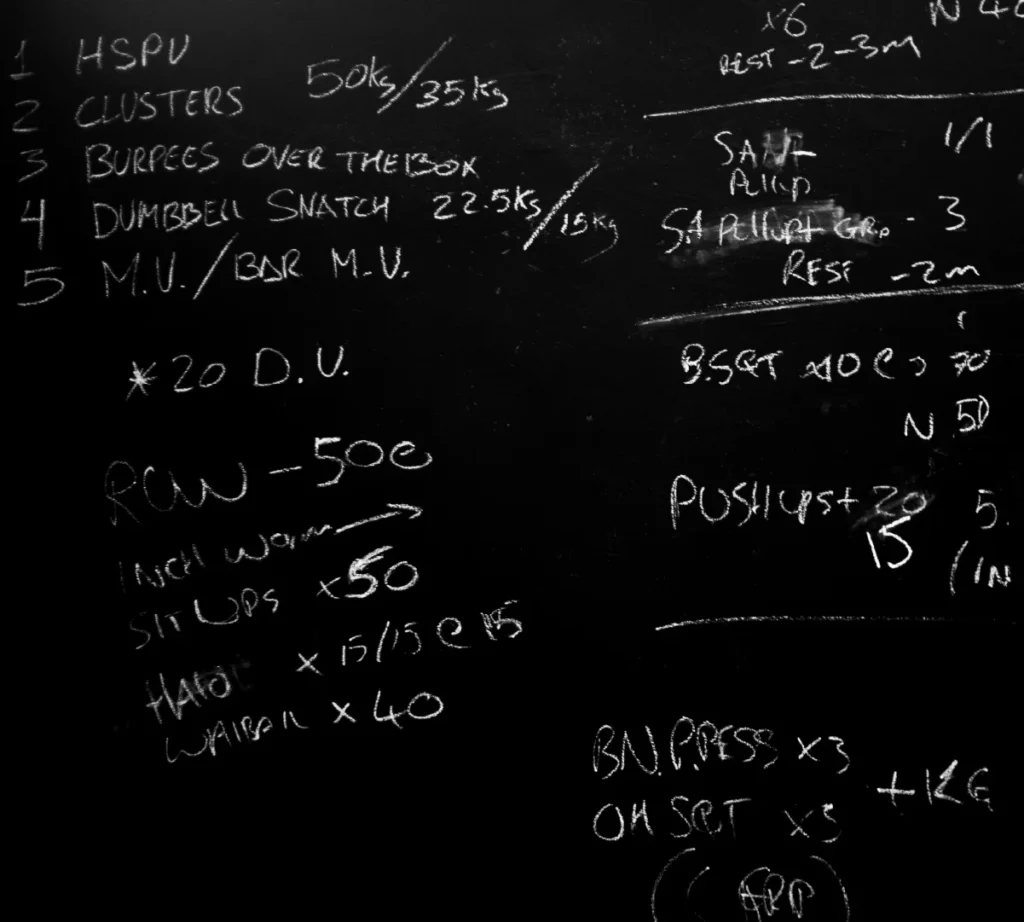 A black chalkboard detailing the workout of the day written in chalk.