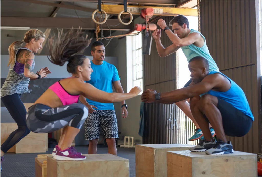 A group of four athletes practice box jumps while their CrossFit coach motivates them during a workout.