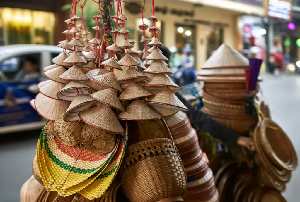 A display of handcrafted woven hats hanging at a vendor booth in a bustling outdoor market.