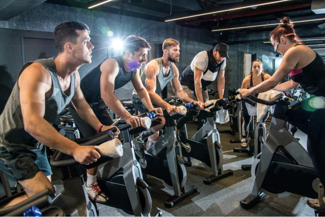 A female instructor teachers spin class students in a gray studio with mirrors and lights.