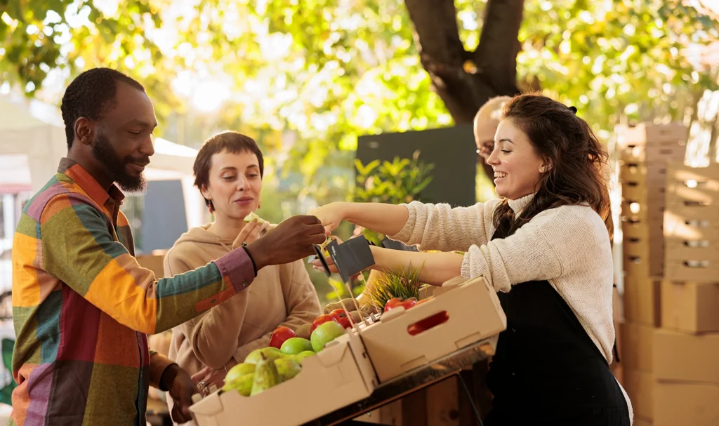 A farmers market vendor is completing a payment with a customer at her outdoor stand.