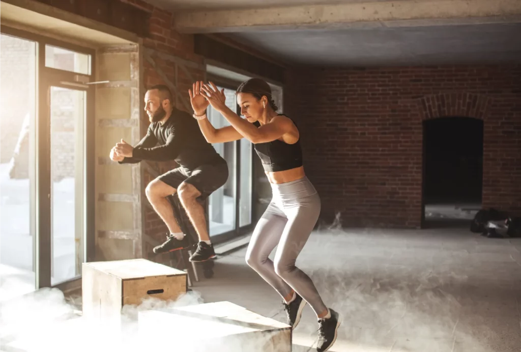 Two people doing box jumps in an empty crossfit gym