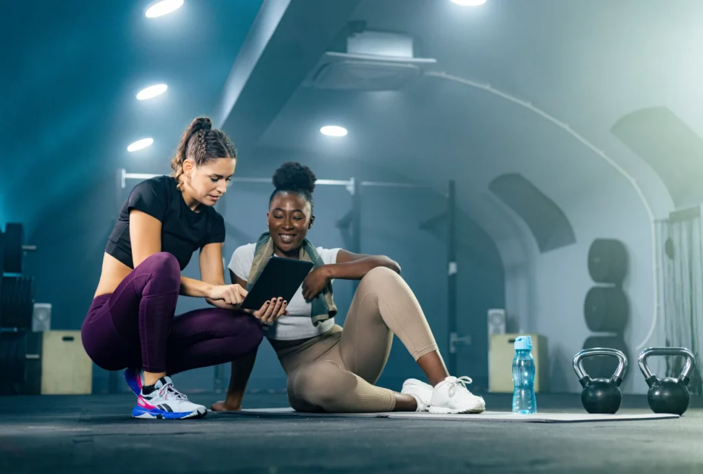 Fitness gym instructor showing a workout plan on tablet to a trainee.