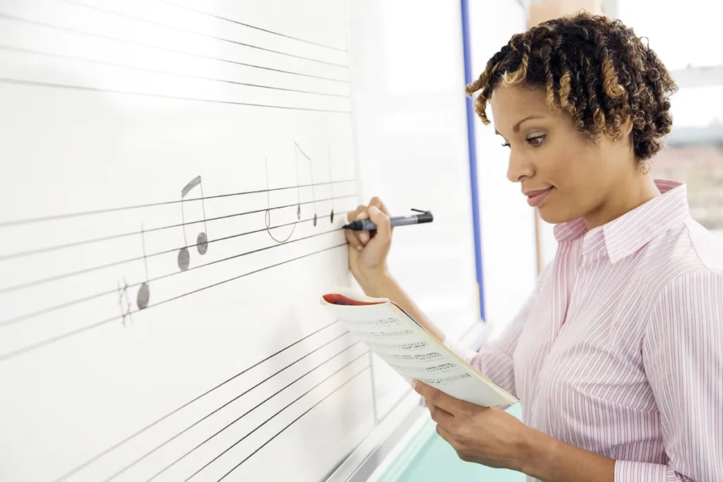 A music teacher writes musical notes on a classroom whiteboard.