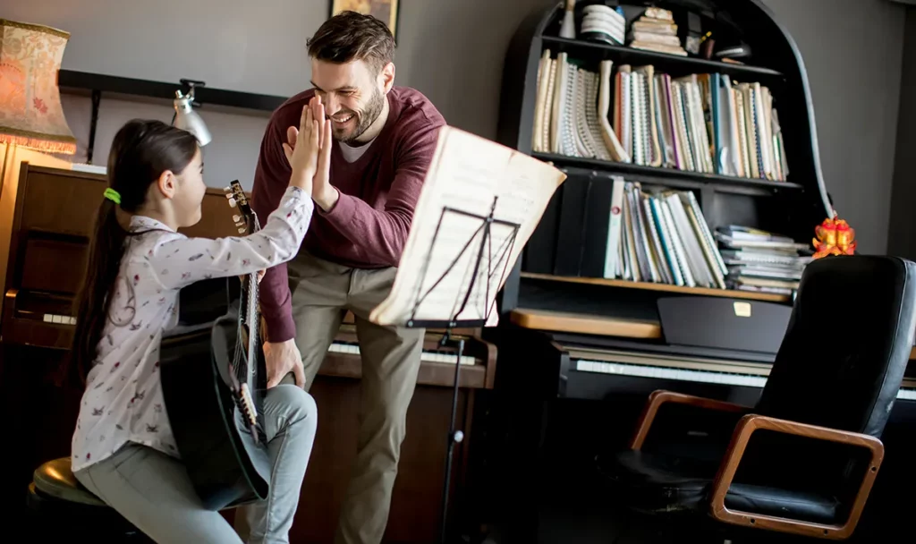 A music teacher high-fives his student during an in-home guitar lesson.