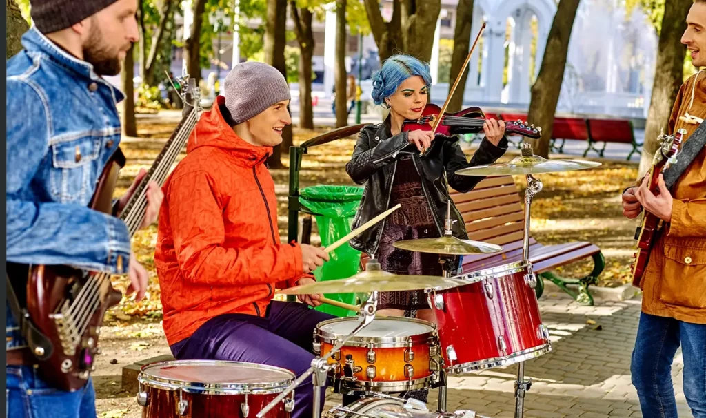 A band consisting of one drummer, two guitarists, and a violinist play outdoors while wearing warm jackets.